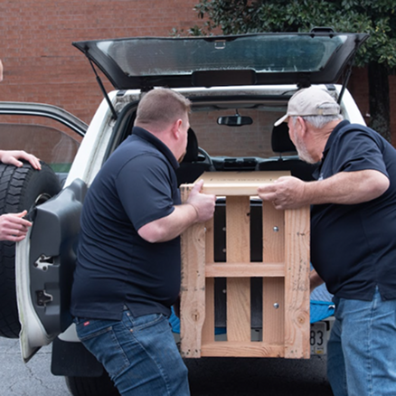 Two men loading a wooden crate into the back of a car