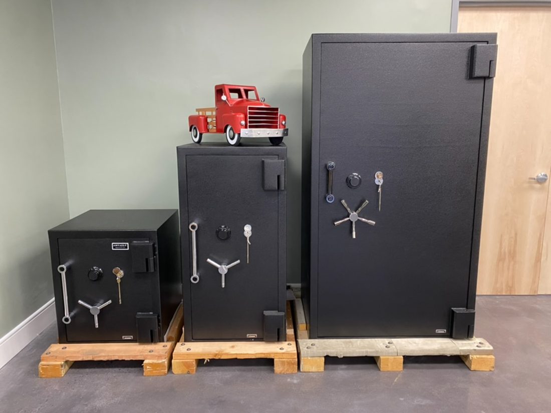 Three black metal safes of different sizes arranged on wooden pallets in an indoor room, with a small red toy truck placed on top of the middle safe.