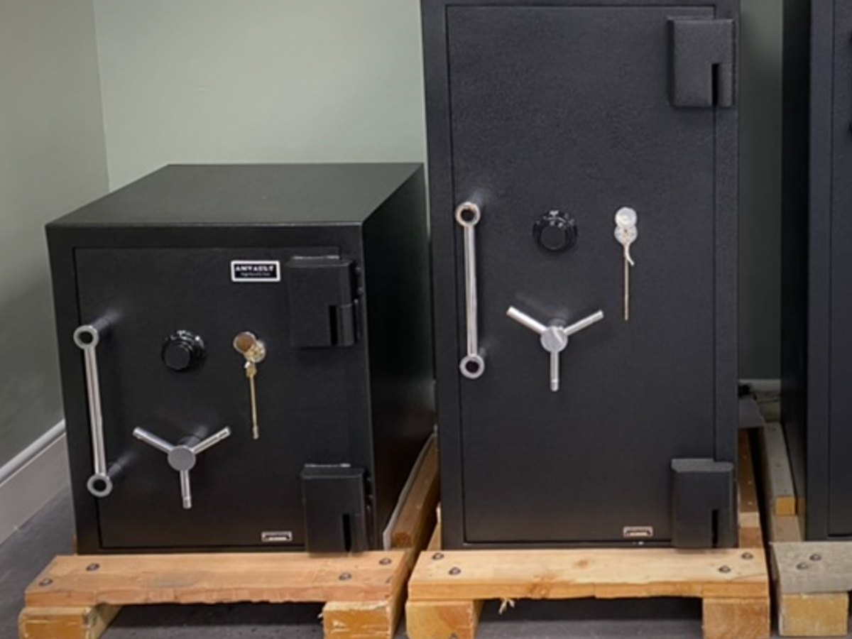 Two black metal safes on wooden pallets, one smaller and one larger, both with silver handles and combination dials in an indoor setting.