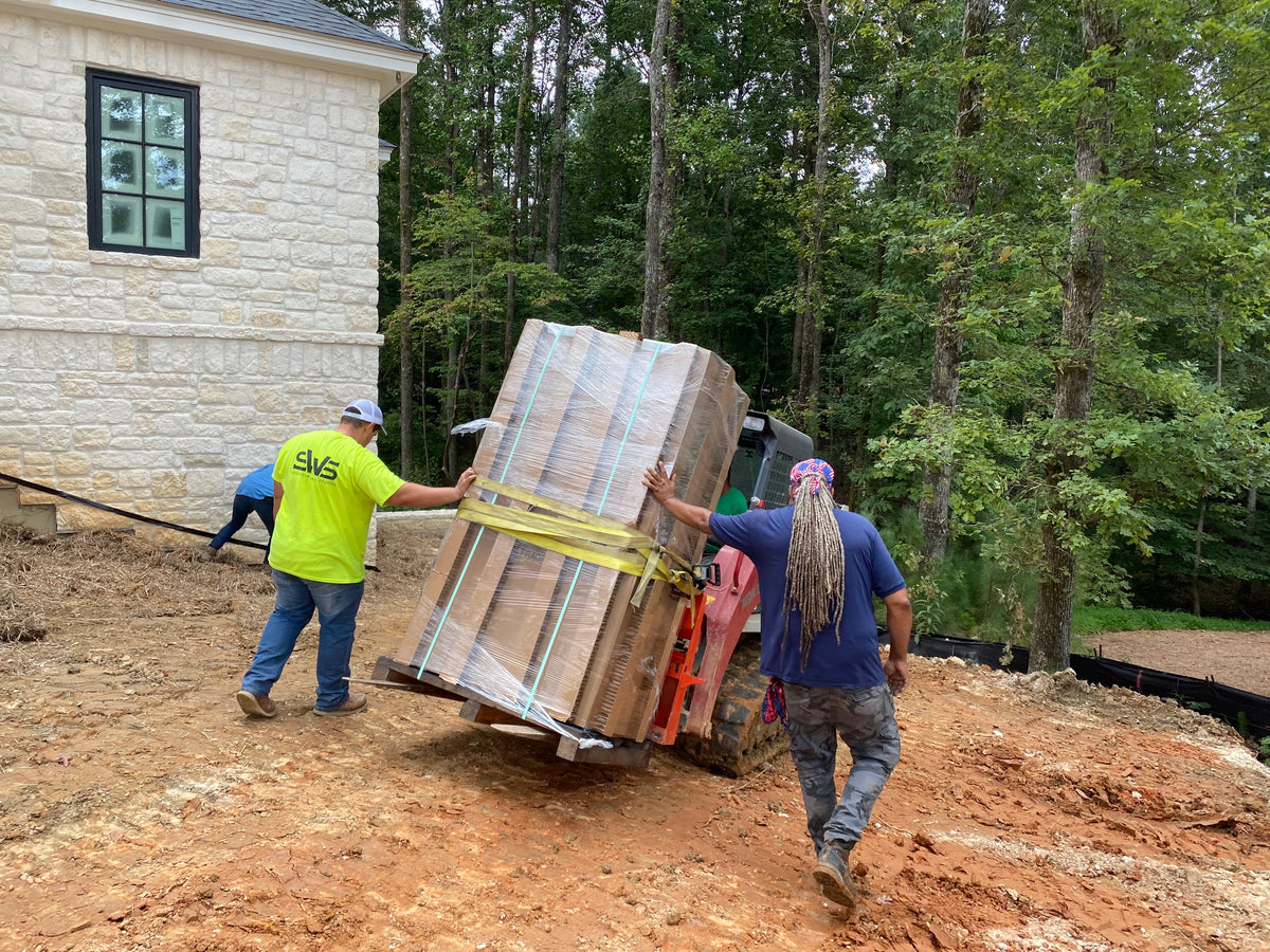 Safe installation crew using a crane to lift a large boxed safe outside a home, showing the equipment and coordination needed for professional installation.