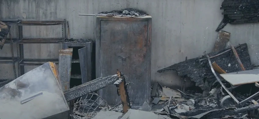 Fire-damaged room with debris and a standing safe against a concrete wall.