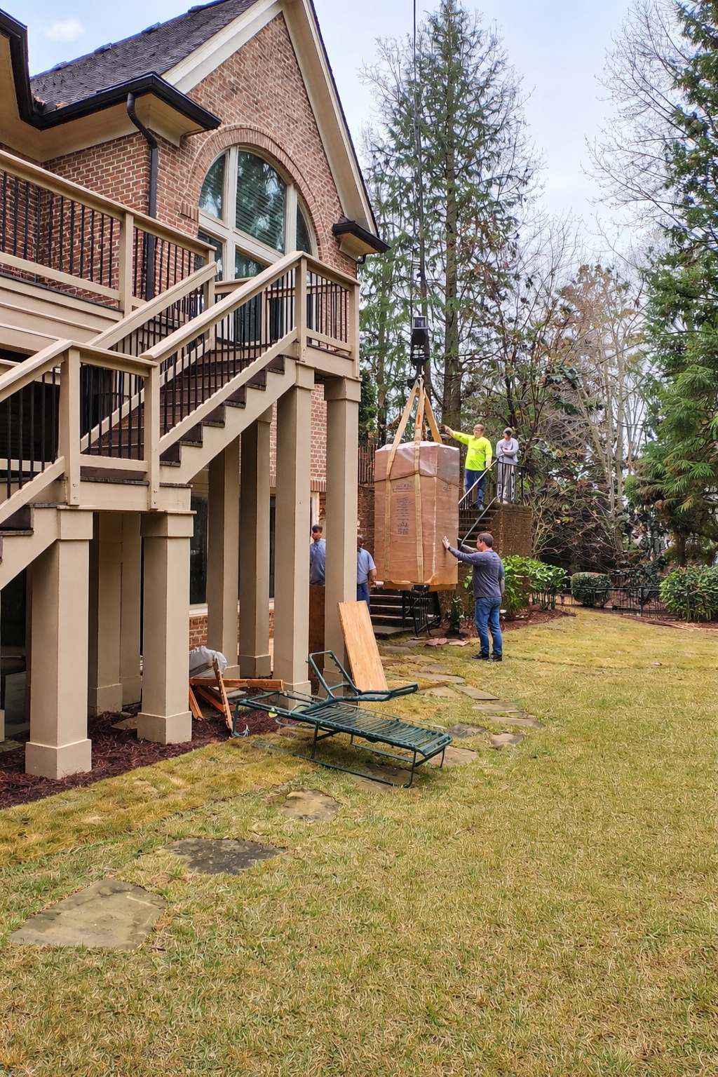 Safe installation crew using a crane to lift a large boxed safe outside a home, showing the equipment and coordination needed for professional installation.
