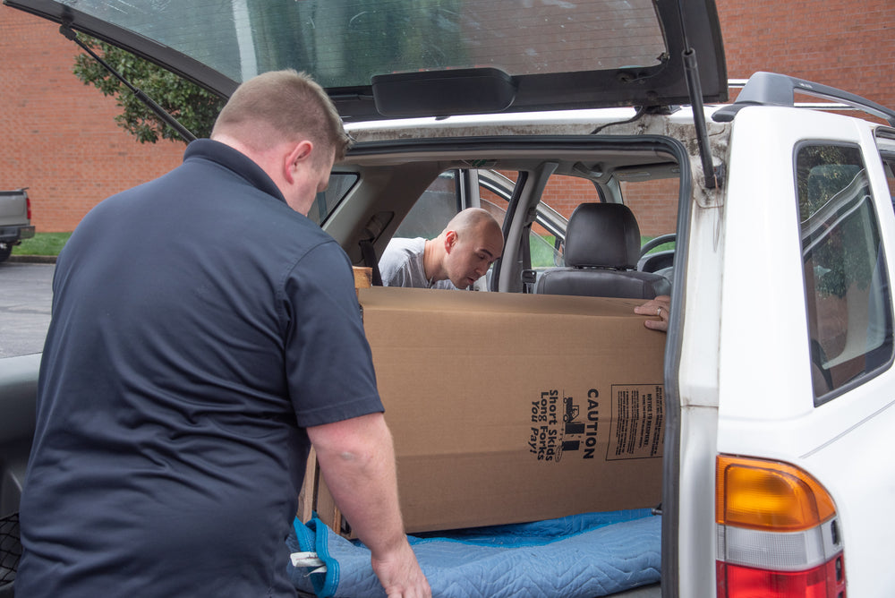 Two movers loading a boxed safe into the back of an SUV, illustrating flexible delivery options based on customer comfort level