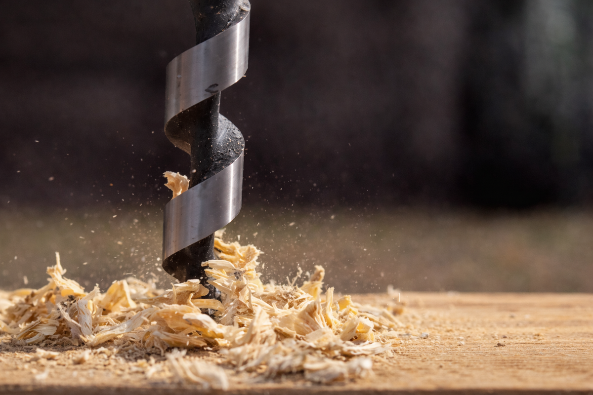Close-up of a drill bit boring into wood with sawdust, representing drilling and anchoring a safe to the floor for theft resistance.