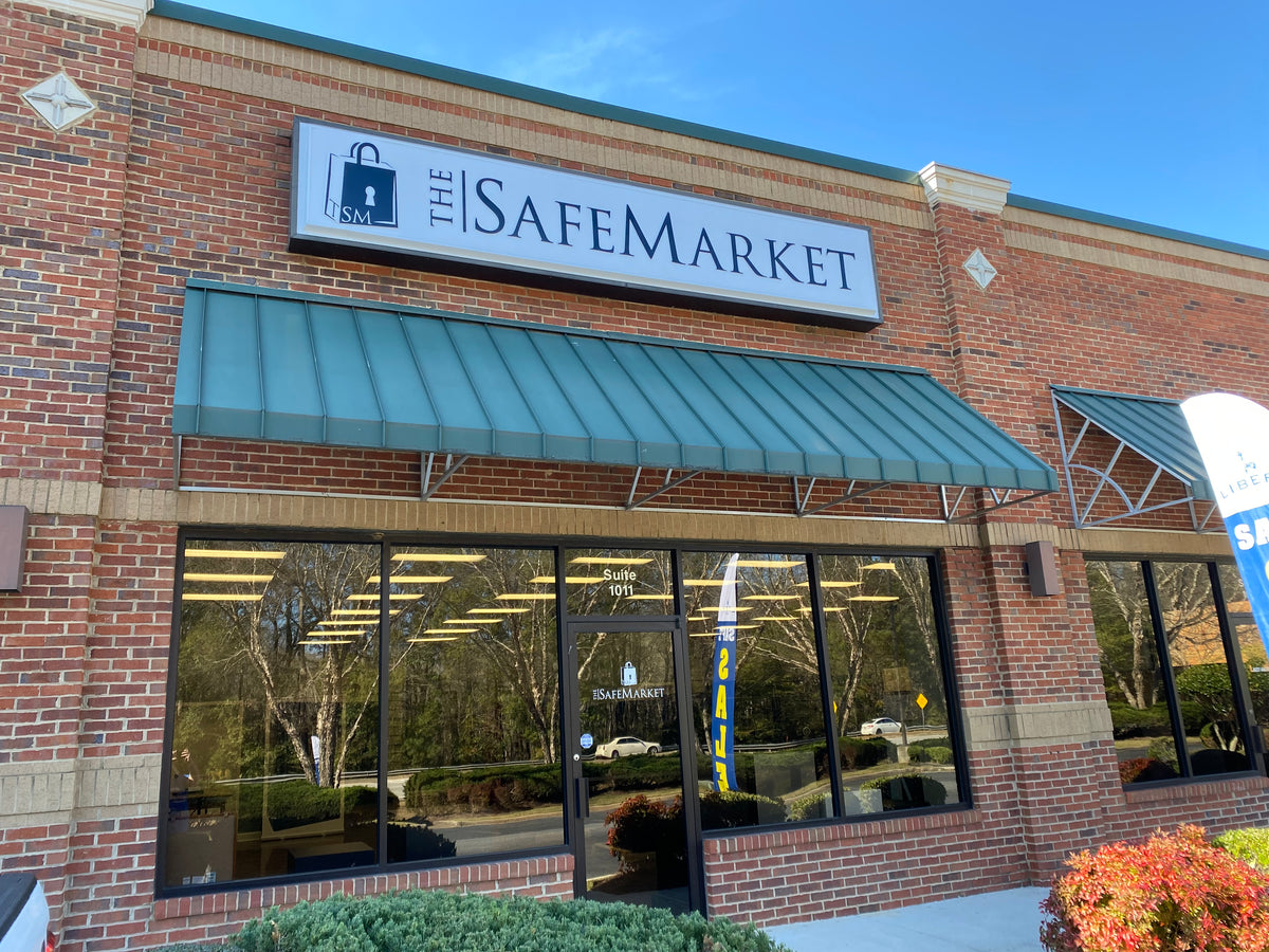 The Safemarket retail store exterior featuring a red brick facade, a green metal awning, a large white sign with the store name, and large glass windows.